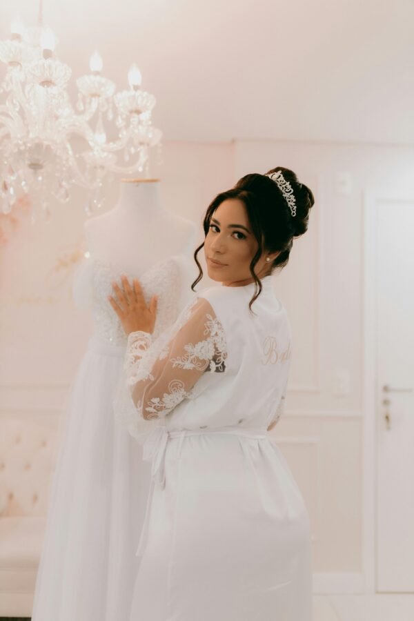 Bride in lace robe with wedding dress in elegant room, showcasing bridal elegance.